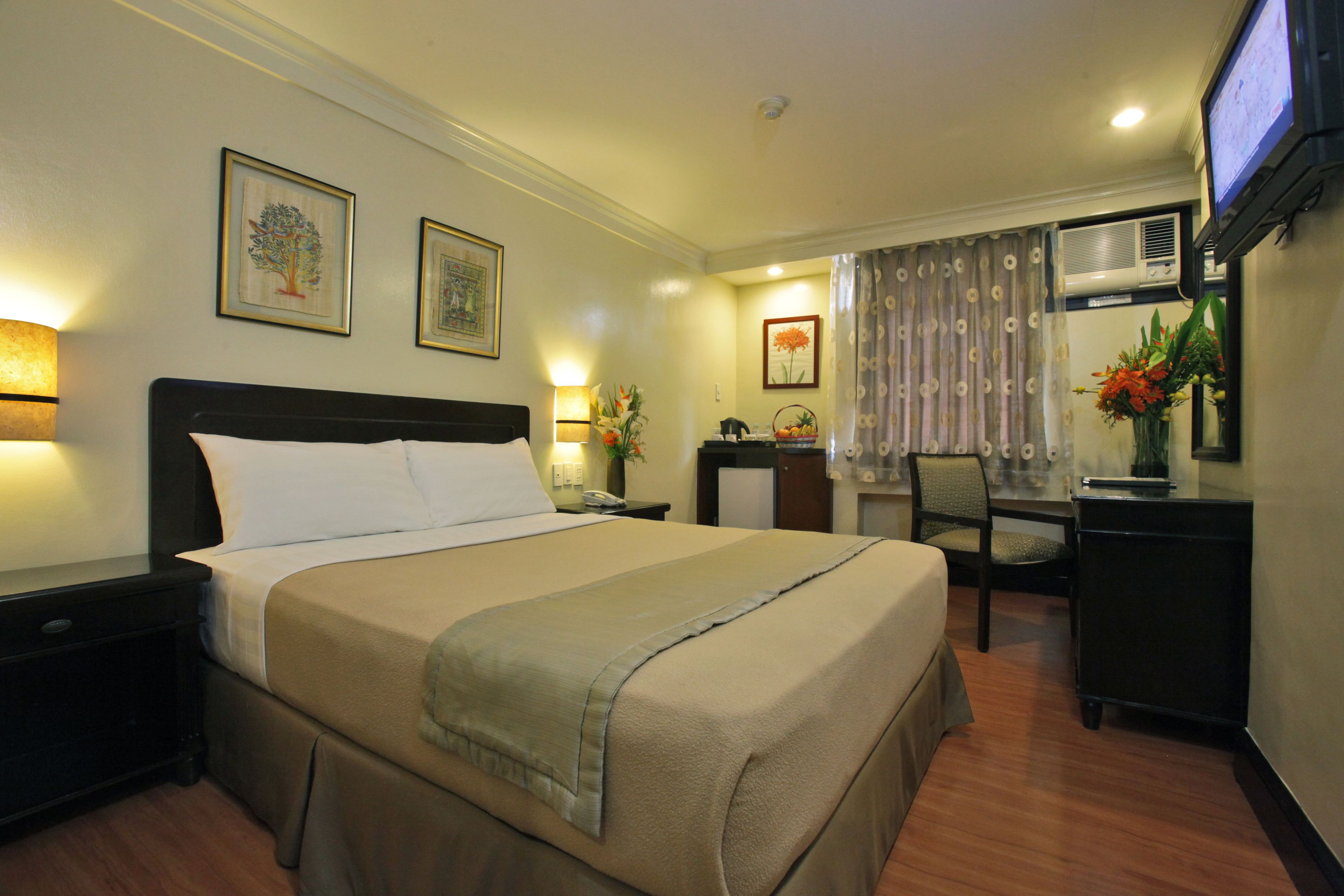 A hotel room with a large bed, a desk with a chair, a television, and artwork on the walls.