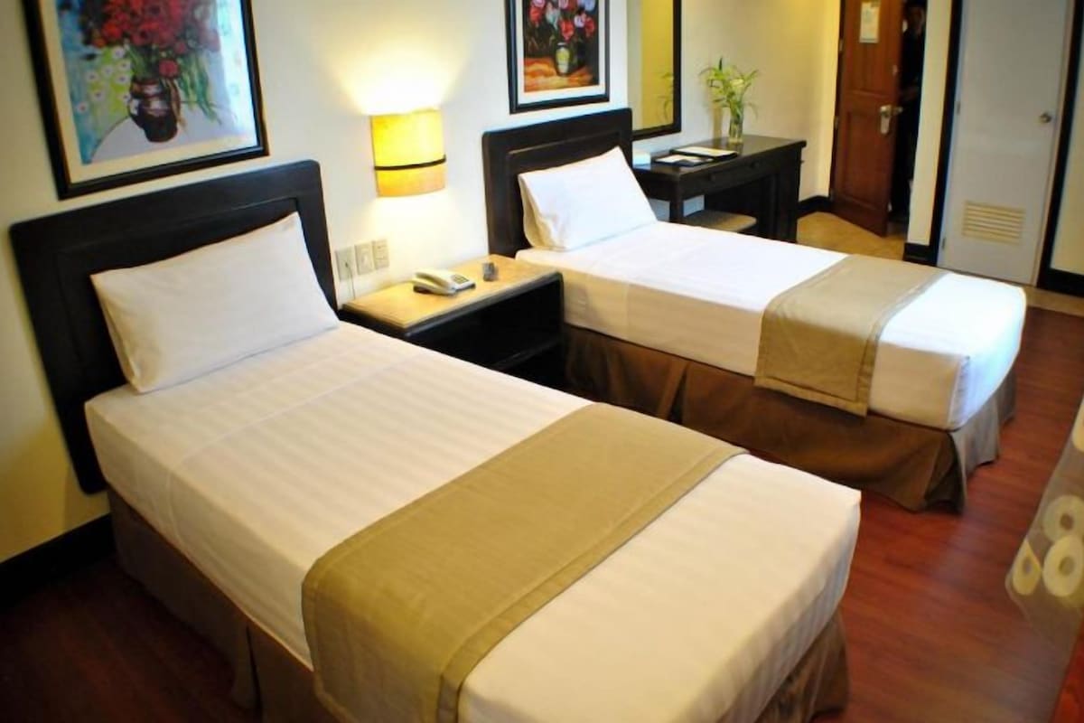 Una habitación de hotel con dos camas, mesitas de noche, lámparas y una puerta.