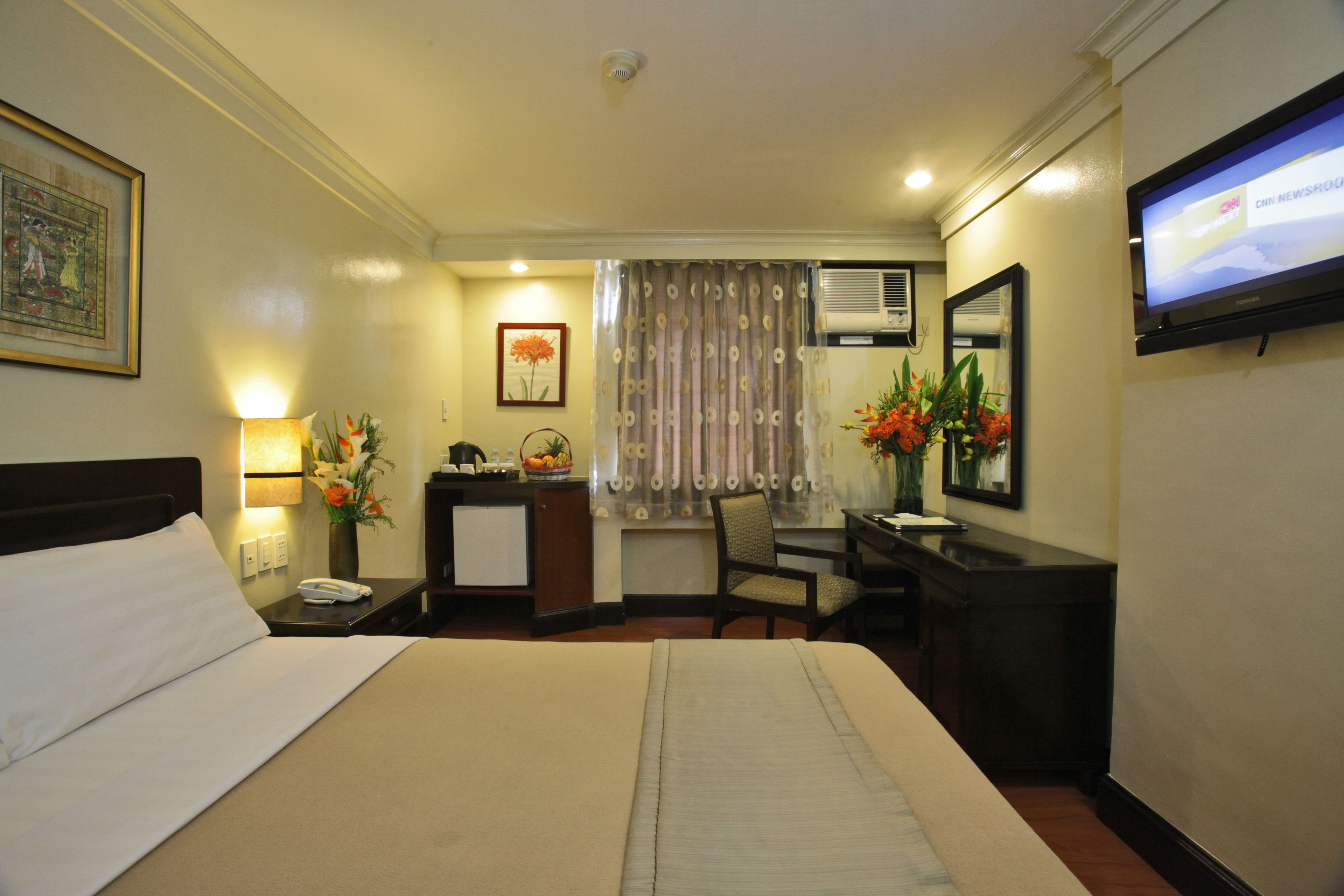 A hotel room with a large bed, a desk, a chair, a TV, and a window with curtains.