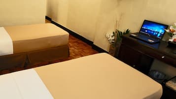 A hotel room with two beds, a television mounted on the wall, and a laptop on a desk.