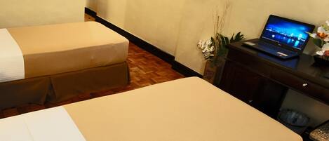 A hotel room with two beds, a television mounted on the wall, and a laptop on a desk.