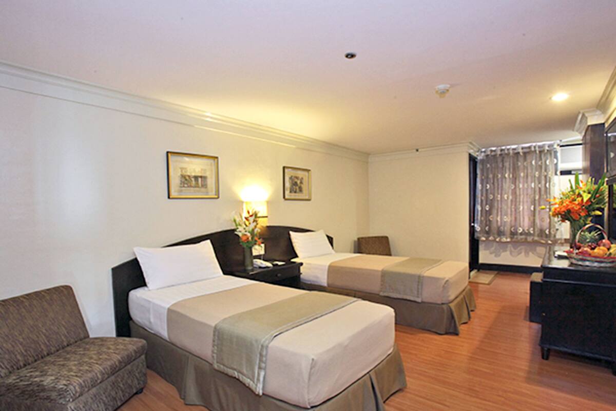 A hotel room with two beds, a sofa, a desk with a lamp, and a window with curtains.