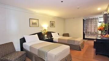 A hotel room with two beds, a sofa, a desk with a lamp, and a window with curtains.