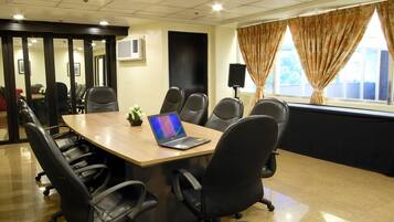 Un salón de conferencias con una larga mesa, sillas de oficina negras, una computadora portátil y un altavoz.