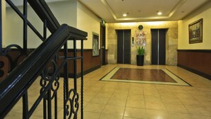 A hotel lobby with a staircase, elevators, a clock, and a potted plant. - Fersal Hotel Malakas (Quezon City)