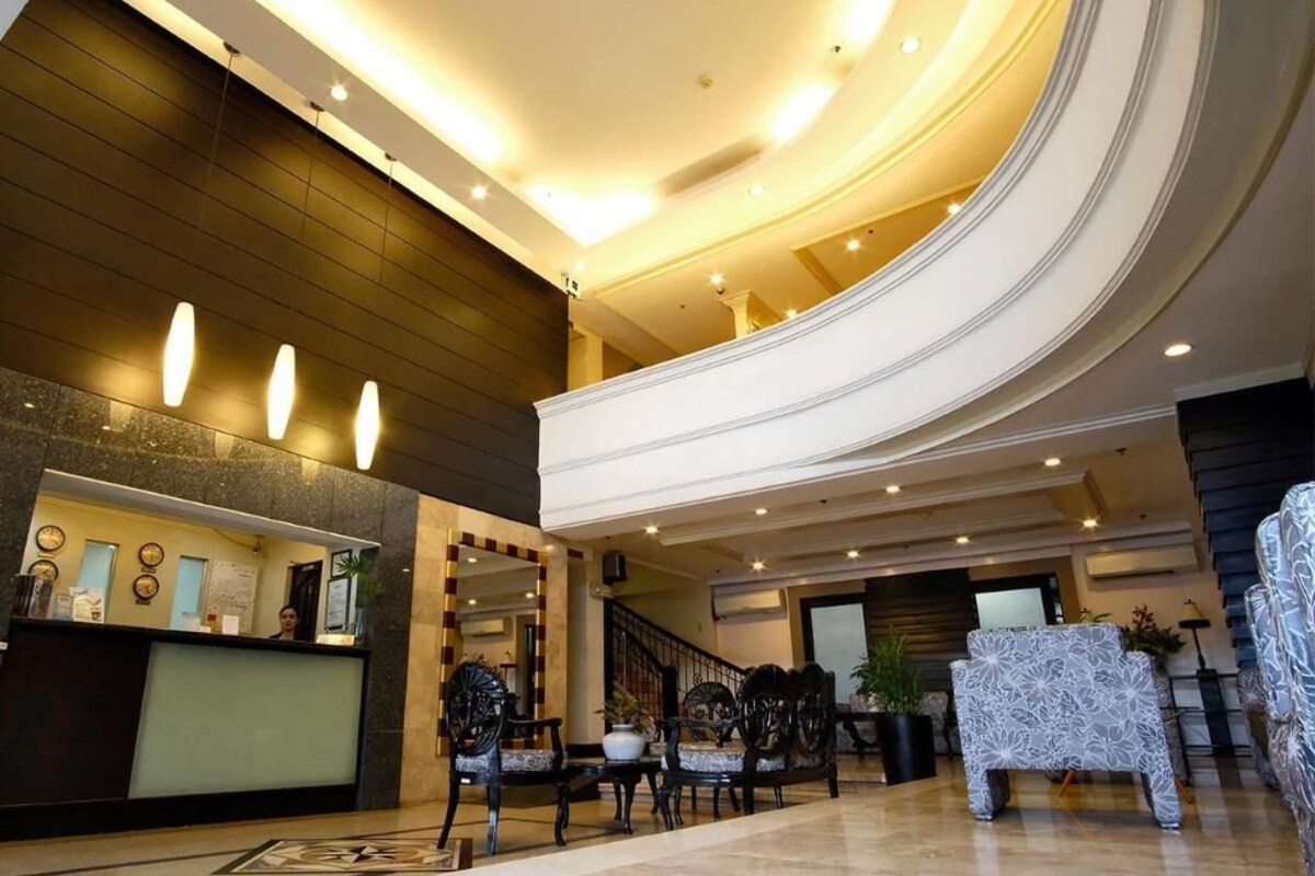 Vestíbulo de hotel con recepción, zona de estar, escalera y un techo alto con iluminación empotrada.