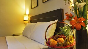 A hotel room with a neatly made bed, a bedside table with a fruit basket and a vase of flowers, and two framed pictures on the wall. - Fersal Hotel Malakas (Quezon City)