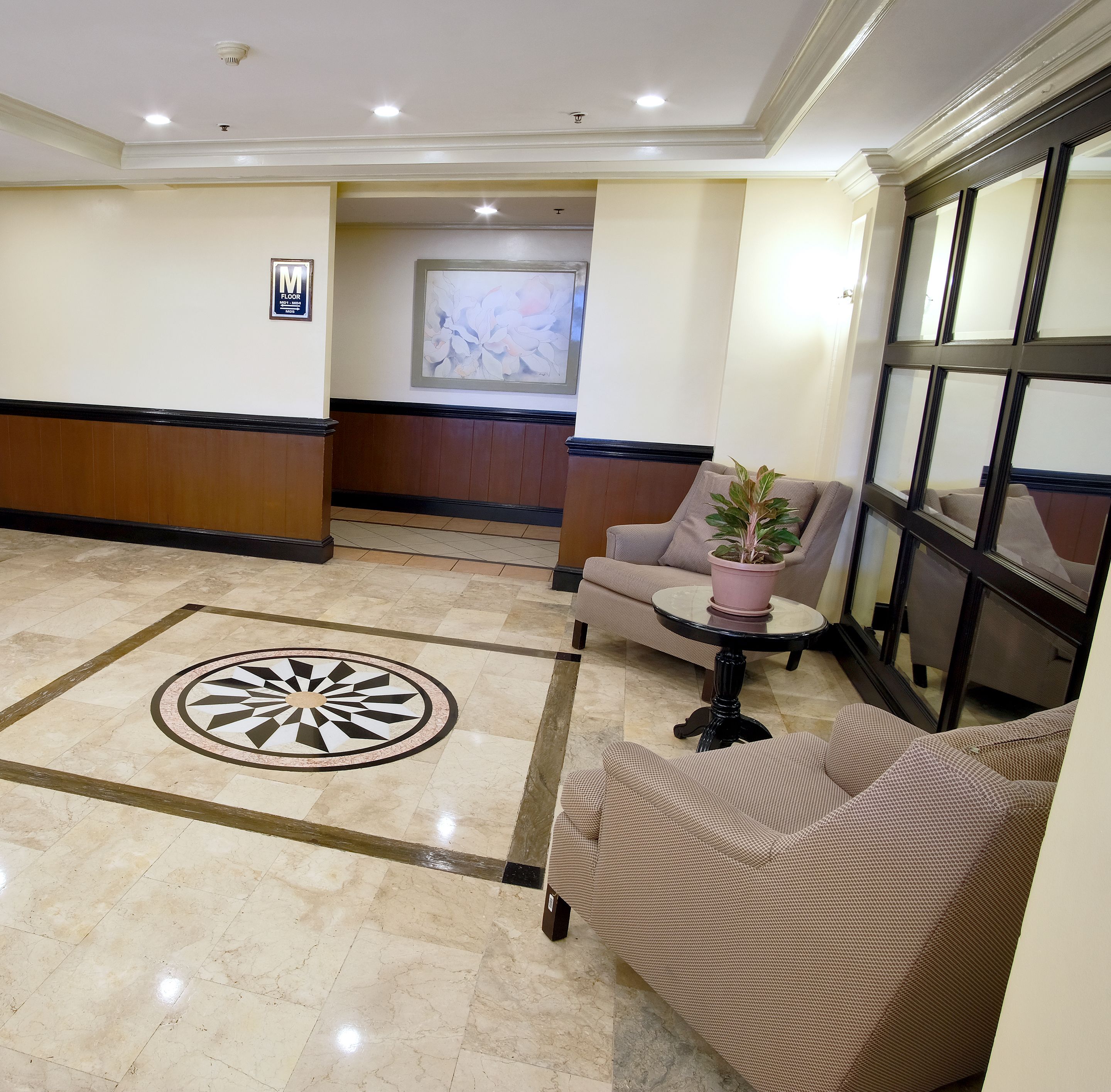 A lobby with a patterned floor, a seating area with a potted plant, and a large window.
