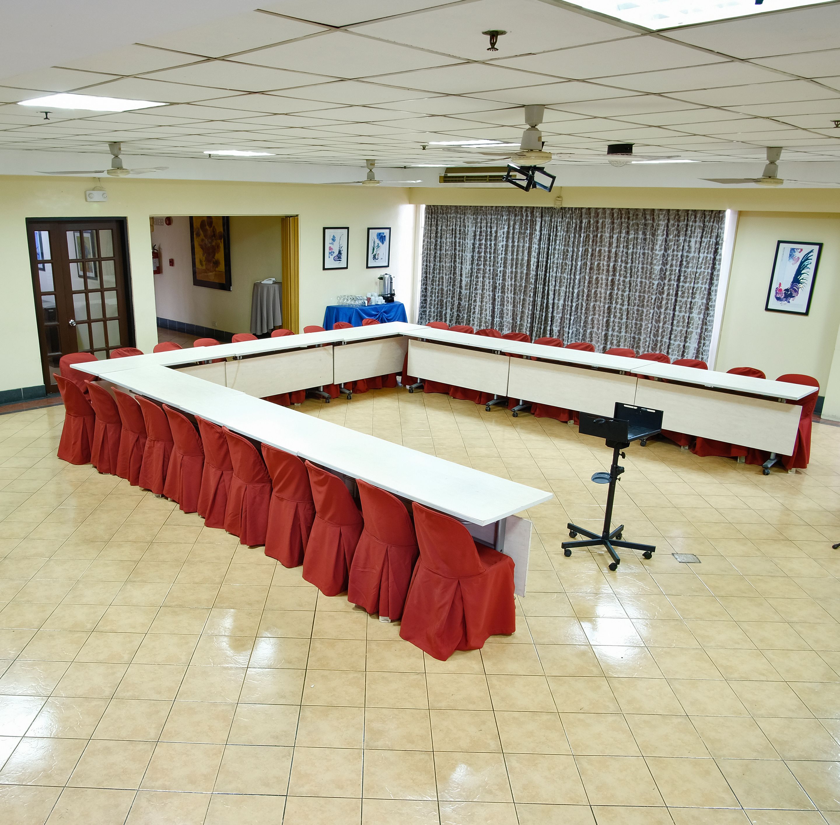 A conference room with a long table, red chairs, a projector, and a ceiling fan.