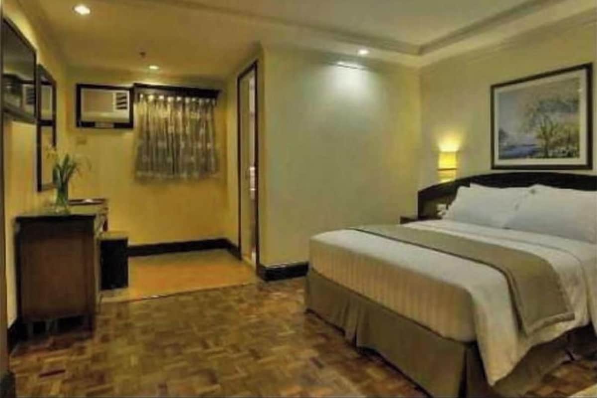Habitación de hotel con cama, escritorio, silla, un cuadro en la pared y ventana.