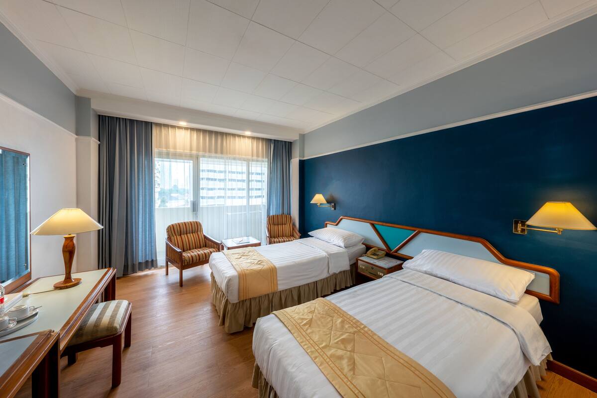 Habitación de hotel con dos camas, un escritorio, una silla y una ventana con cortinas.
