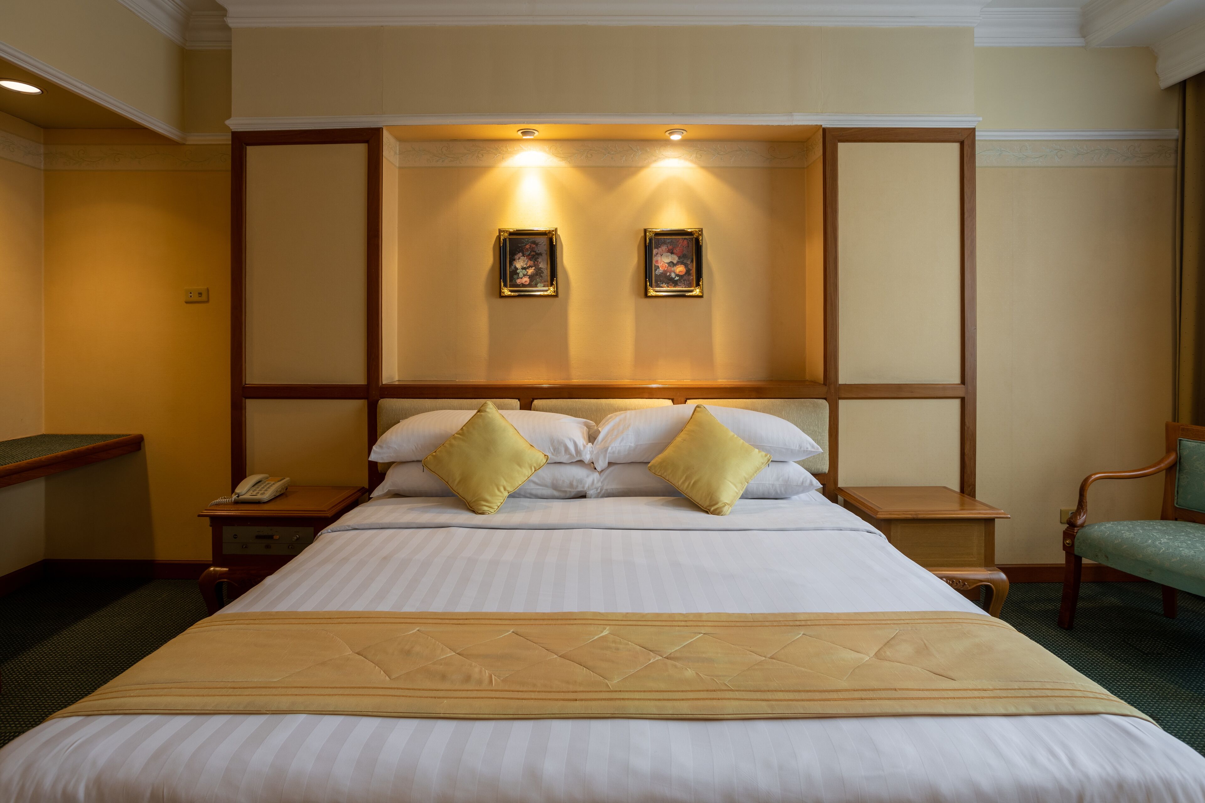 A hotel room with a large bed, two bedside tables, a nightstand, a green chair, and two wall-mounted picture frames.