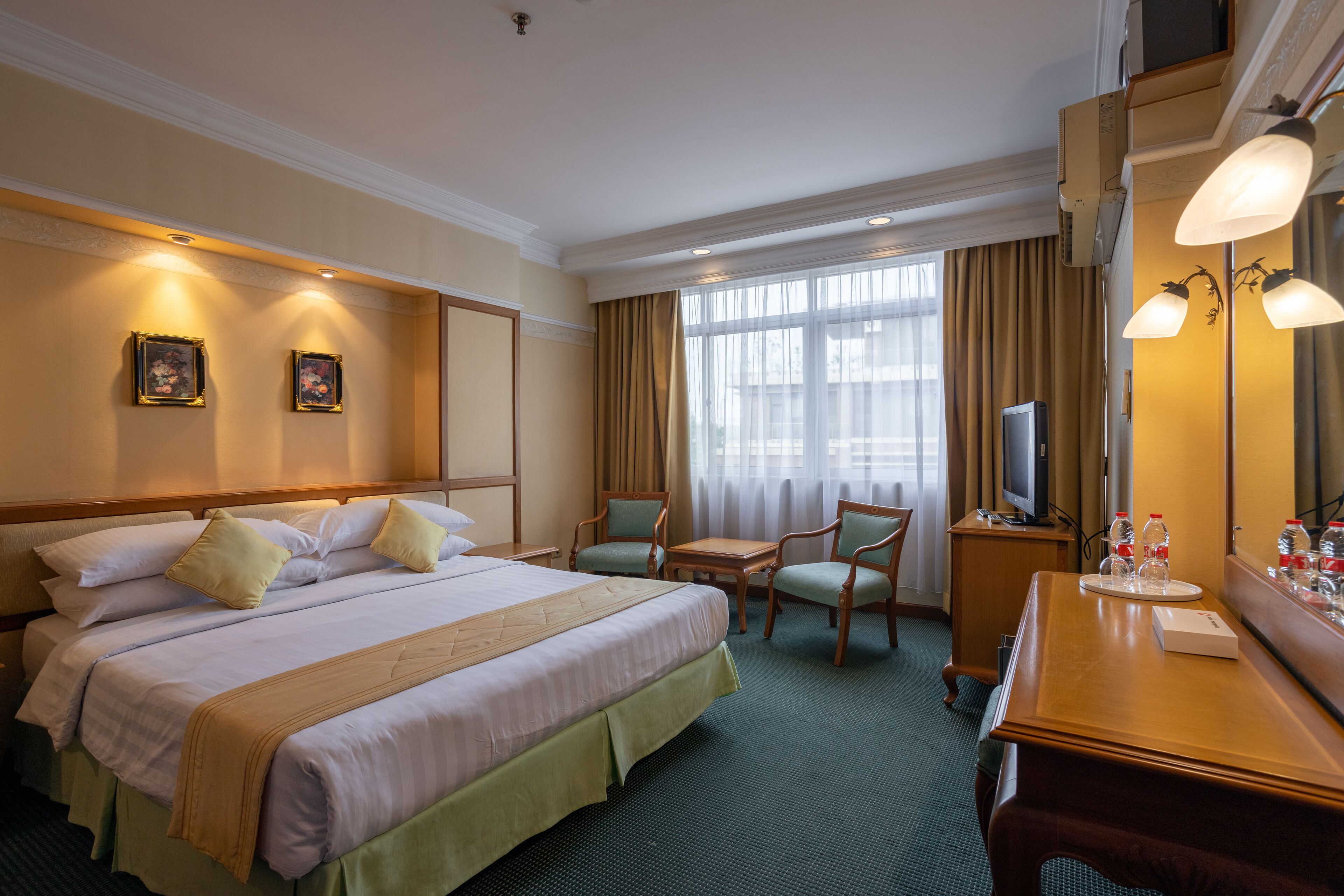 Una habitación de hotel con una cama grande, dos sillas, una mesita, un televisor y un espejo.