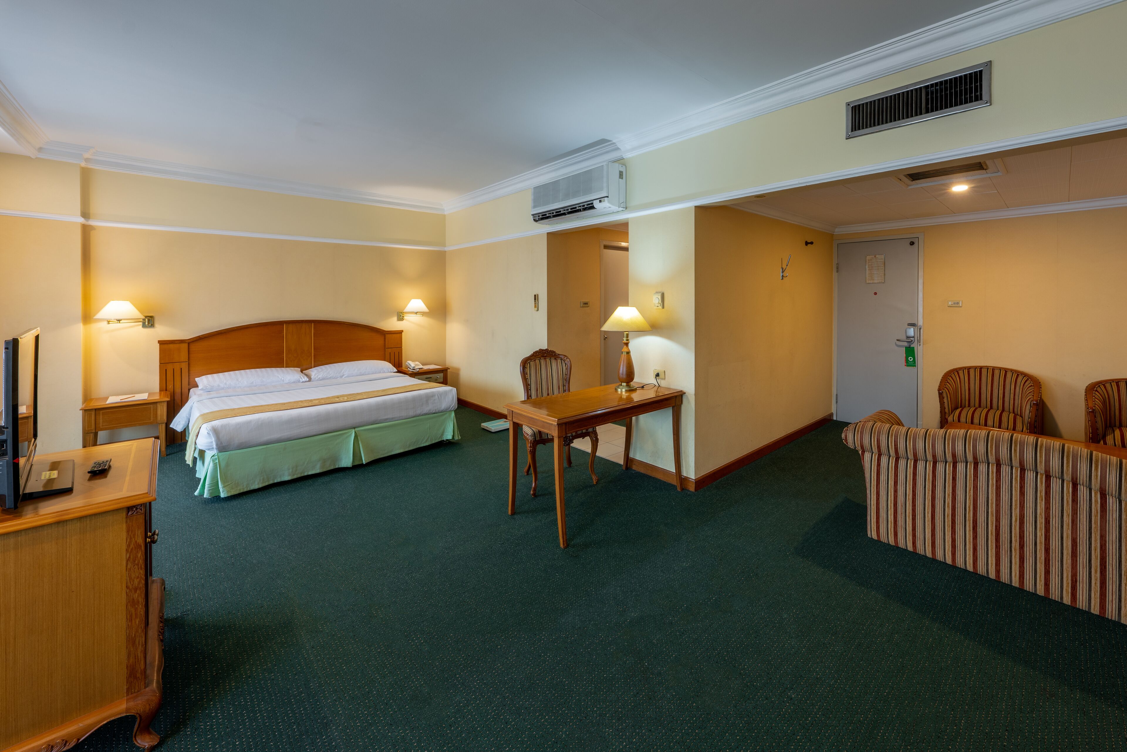 A hotel room with a double bed, a desk with a chair, a small table, and a sofa.
