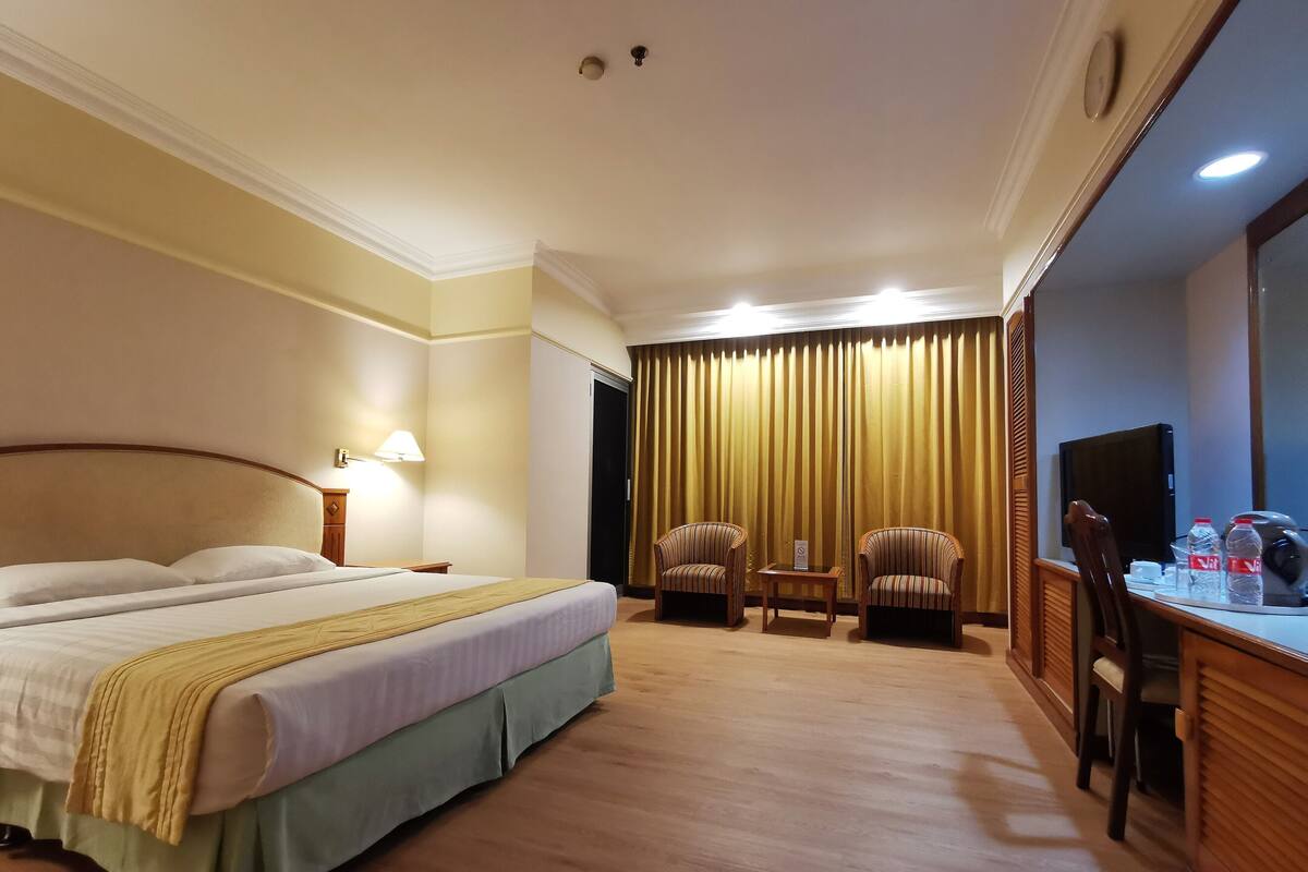 Habitación de hotel con una cama grande, dos sillones, una mesita, un escritorio con computadora y televisión.