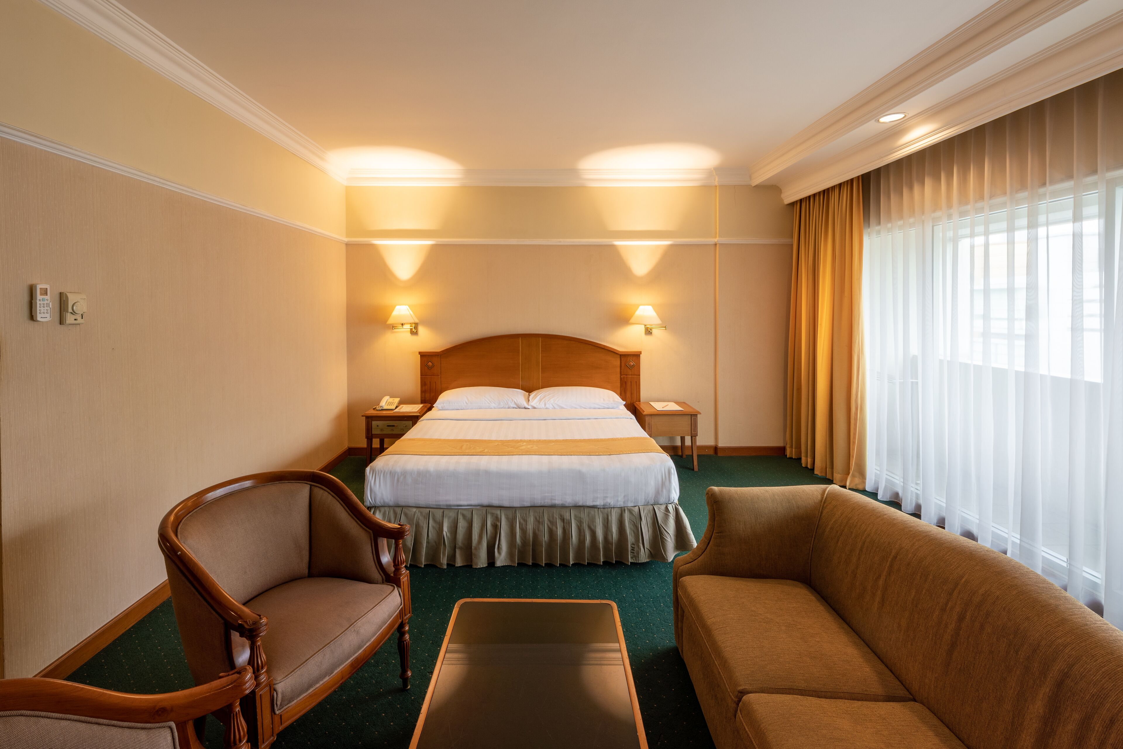 A hotel room with a large bed, two bedside tables, a wooden headboard, a sofa, and a small table.