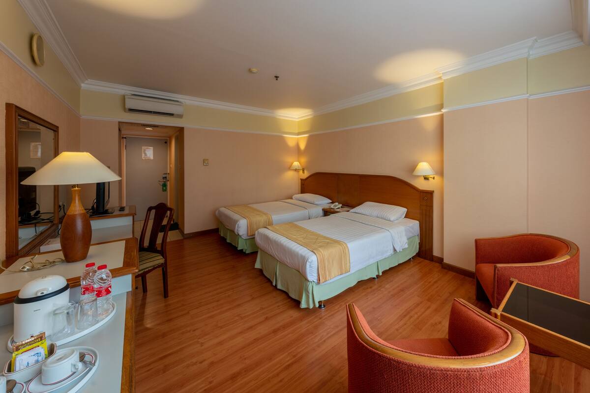 Habitación de hotel con dos camas, un escritorio con lámpara, una silla y una mesita con una bandeja de objetos.