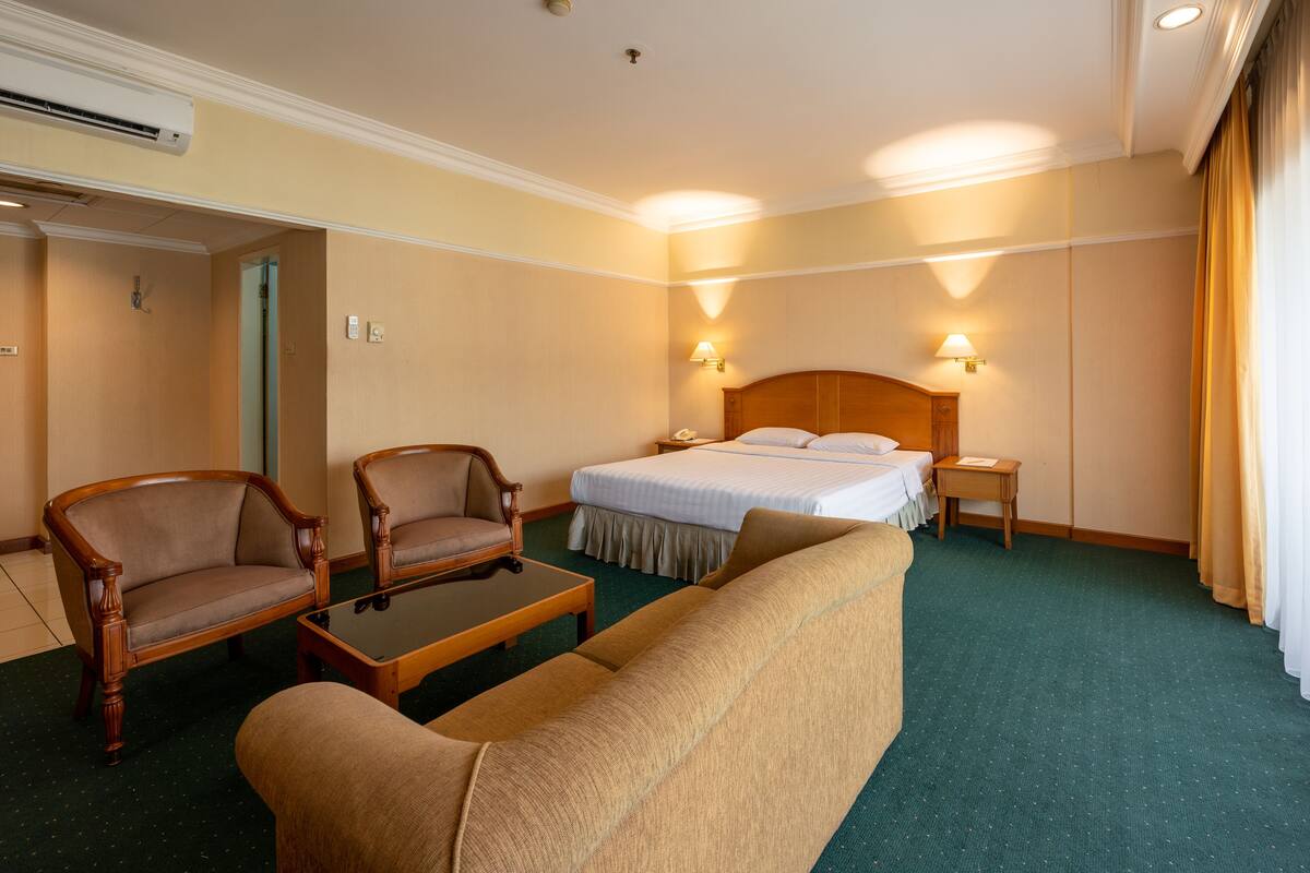 Una habitación de hotel con una cama, dos sillones, una mesita y una mesita de noche.