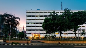 A multi-story hotel with a central entrance, surrounded by a fence and palm trees. - Hotel Marcopolo Jakarta (Jakarta)