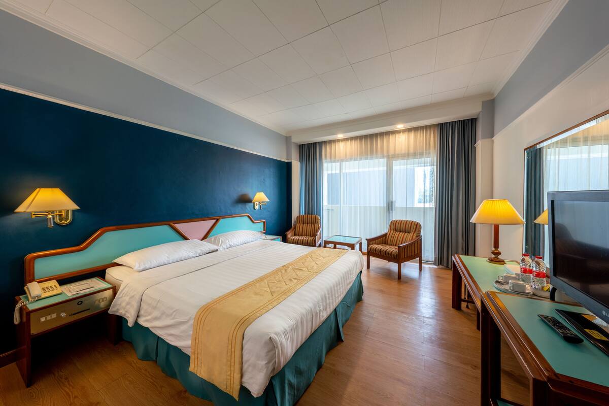Una habitación de hotel con una cama grande, dos sillones, un escritorio con televisor y una ventana con cortinas.
