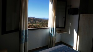A room with a large window, a bed, a small table, and a mirror.