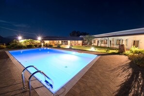 A swimming pool with a metal ladder, surrounded by a paved area and a building with multiple windows and doors. - Agriturismo Irghitula (Posada)