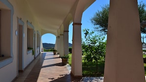 A covered corridor with columns, potted plants, and a view of greenery and hills in the distance.