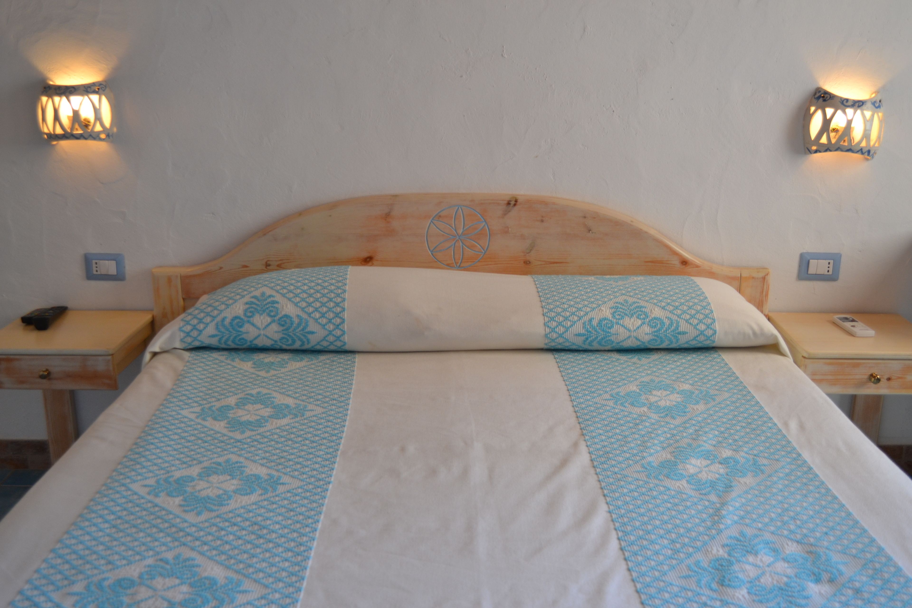 A bed with a wooden headboard, two bedside tables, and wall-mounted light fixtures.