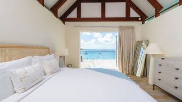 Un dormitorio con una cama grande, cabecera de madera, cómoda y vistas al mar desde un balcón.