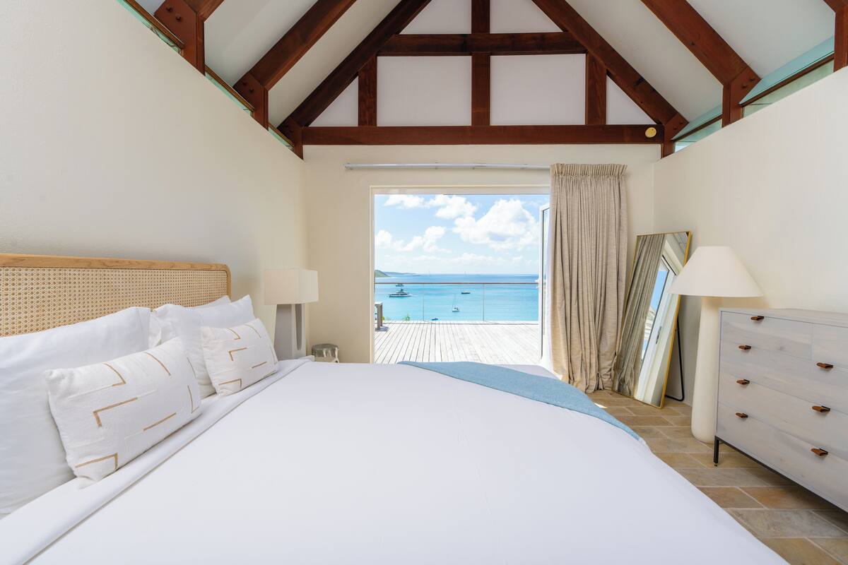 A bedroom with a large bed, a dresser, and a view of the sea.