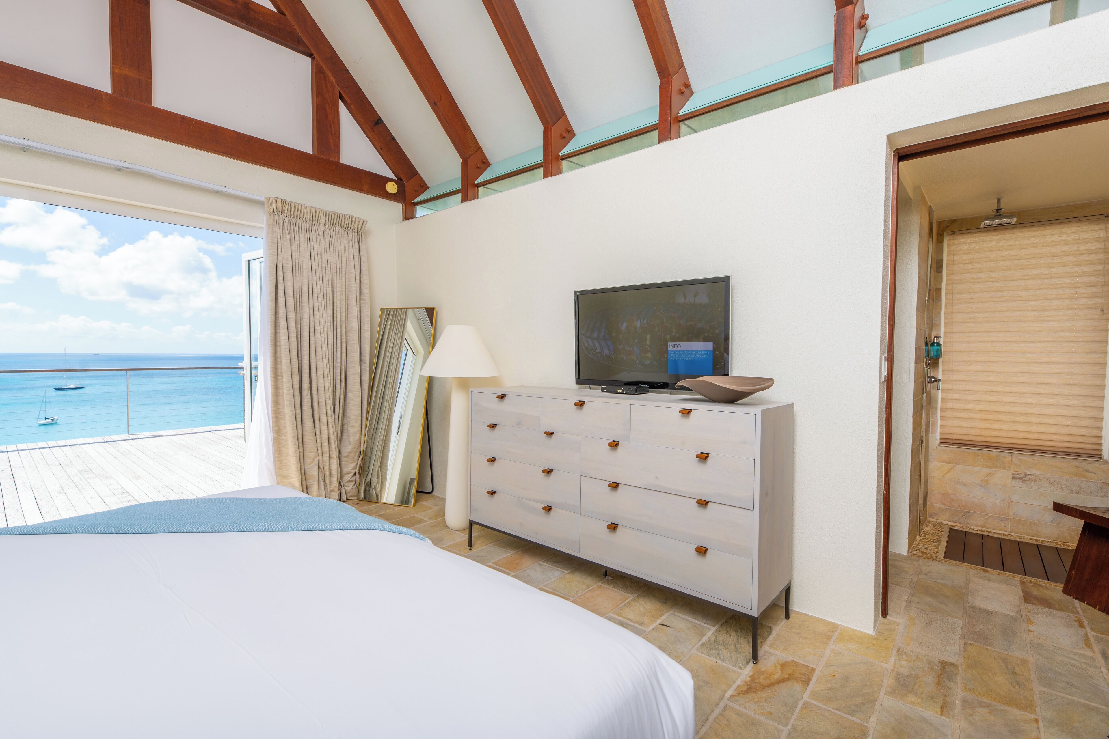 Un dormitorio con cama, televisión, cómoda y vista al mar.