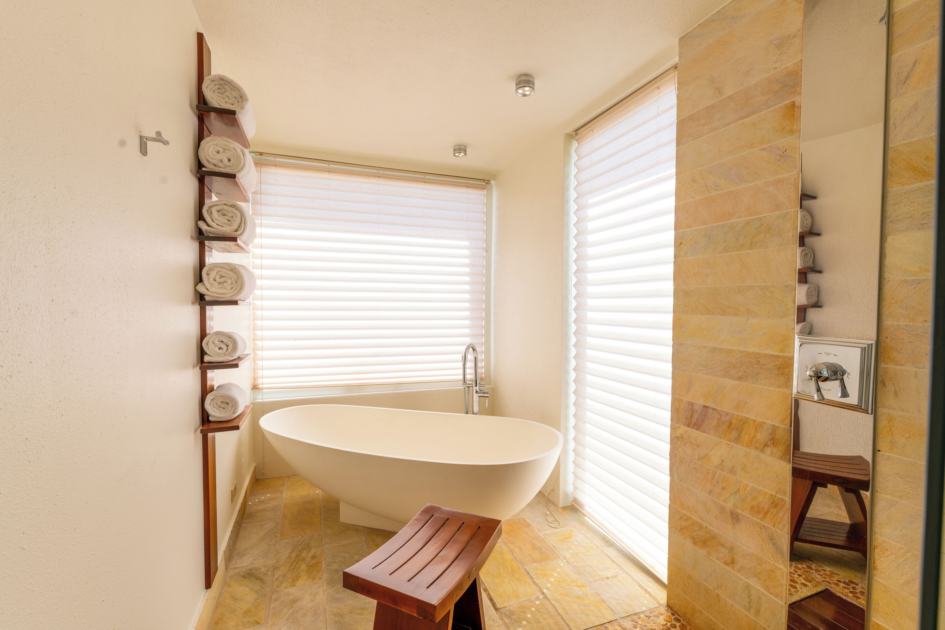 A modern bathroom with a freestanding bathtub, a wooden bench, and a towel rack with neatly rolled towels.