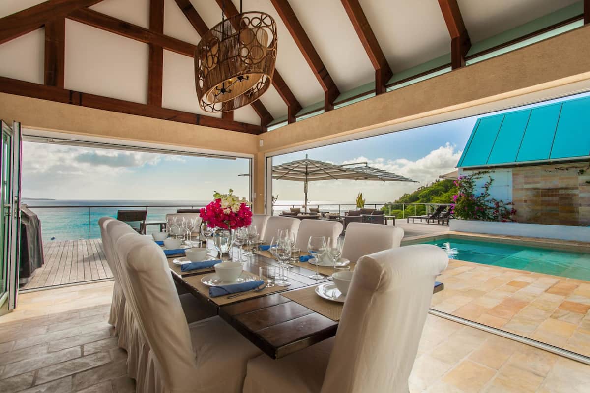 A dining area with a view of the ocean, a pool, and outdoor furniture.