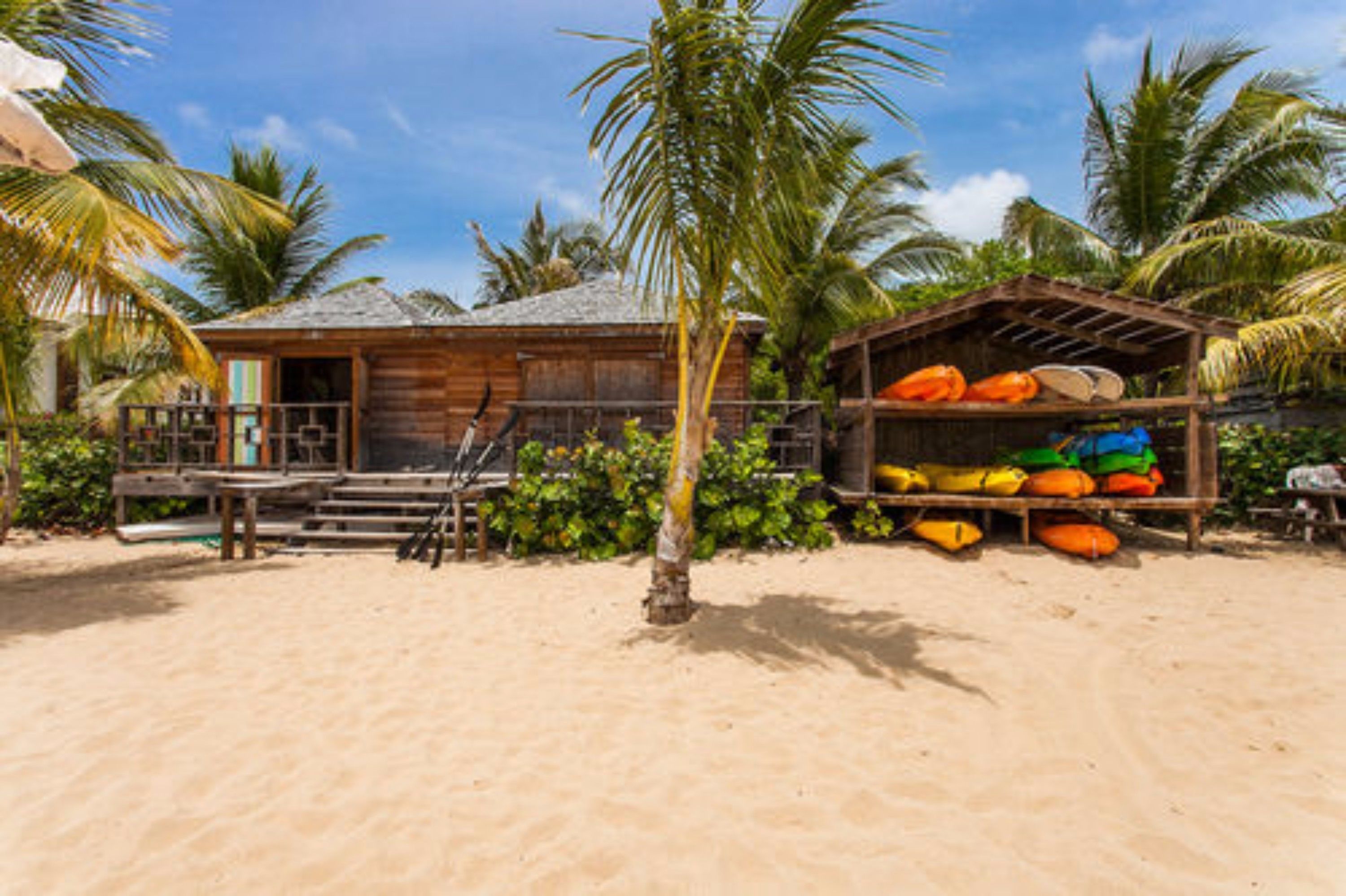 A wooden beach house with a porch and a small shed with colorful kayaks.