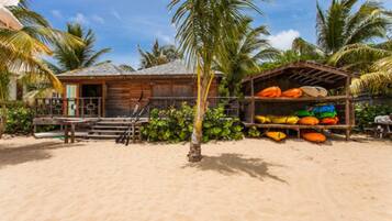 A wooden beach house with a porch and a small shed with colorful kayaks.
