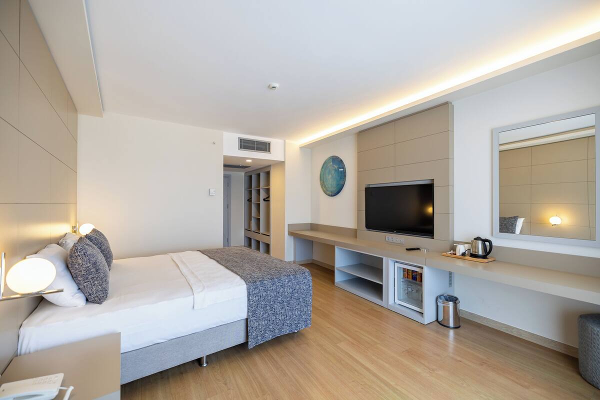 A modern hotel room with a bed, bedside table, TV, and built-in shelves.