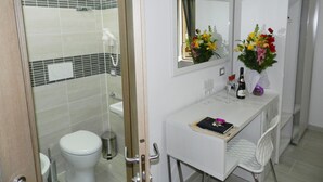 A bathroom with a toilet, shower, and a vanity with a mirror, flowers, and a bottle. - Vatican Rome B&B (Rome)