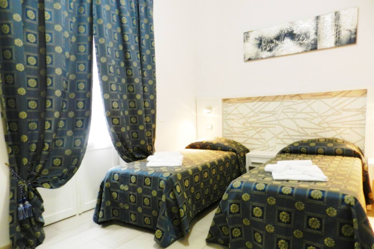 Una habitación de hotel con dos camas individuales, un ventanal con cortinas y una obra de arte colgada en la pared.