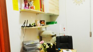 A small office with a desk, a black office chair, a grey sofa, and a bookshelf with various items. - Vatican Rome B&B (Rome)