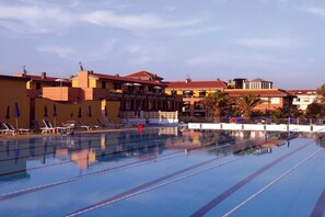 A swimming pool with lounge chairs and a building with multiple balconies in the background. - Continental Resort (Pisa)