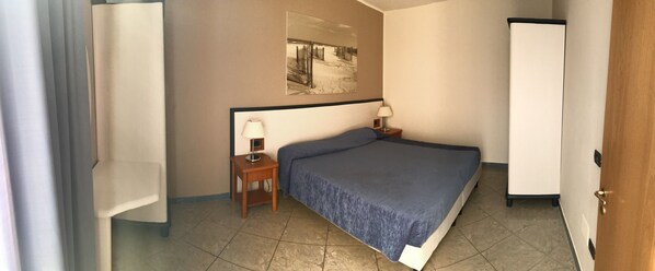 A hotel room with a bed, a nightstand with a lamp, a wall-mounted artwork, and a door.