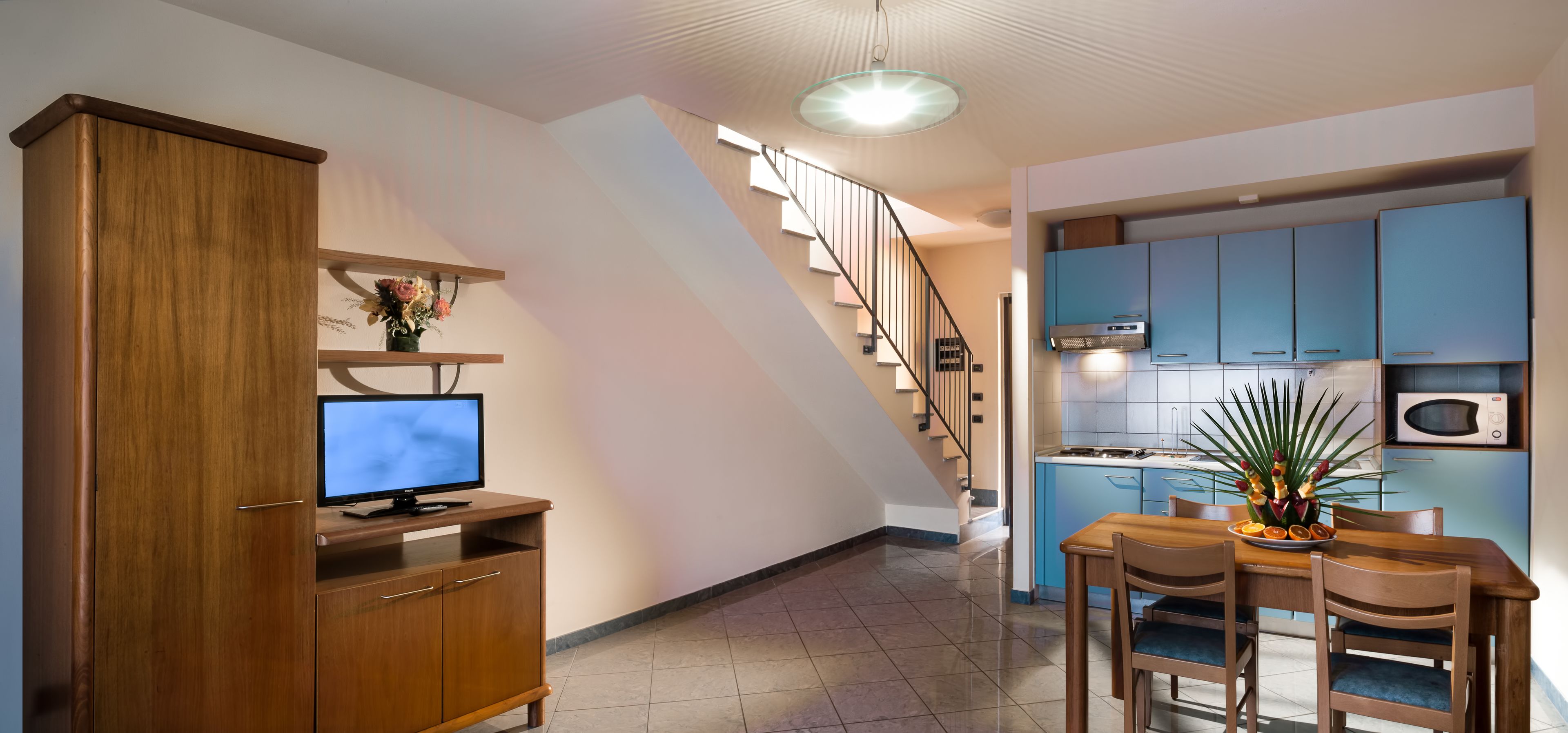 Eine moderne Küche mit blauen Schränken, ein Essbereich mit Holztisch und -stühlen sowie eine Treppe, die zu einer anderen Ebene führt.