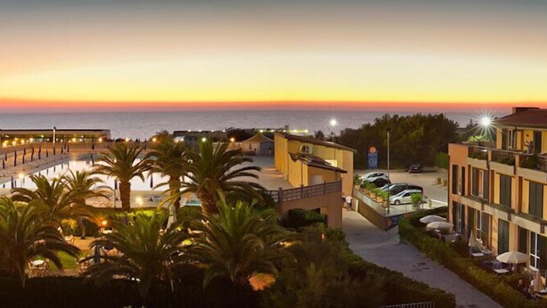 A hotel with a view of the sea at sunset, featuring a pool area and outdoor seating. - Continental Resort (Pisa)
