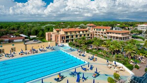 A large swimming pool with multiple lanes, surrounded by lounge chairs and umbrellas, and a hotel building with multiple floors and balconies. - Continental Resort (Pisa)