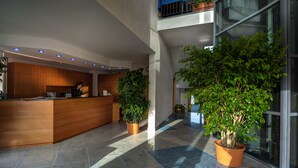 A modern reception area with a wooden counter, potted plants, and a glass wall. - Continental Resort (Pisa)