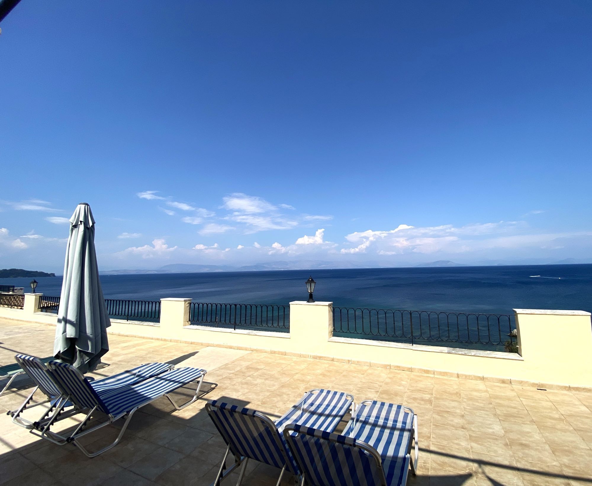 A terrace with lounge chairs and a table, overlooking a body of water and distant land.