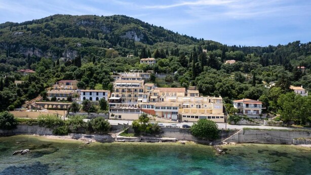 A coastal town with buildings on a hillside, clear waters, and a mountainous backdrop. - El Greco Hotel by Estia (Corfu)