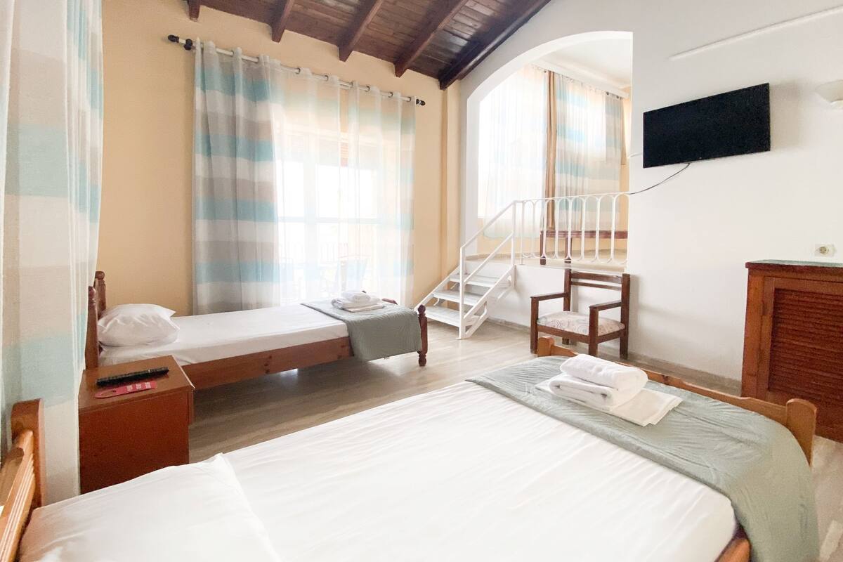 A bedroom with a single bed, a chair, a small table, a TV, and a staircase.