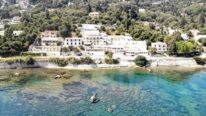 A coastal town with buildings along the shore, clear water, and a rocky beach. - El Greco Hotel by Estia (Corfu)