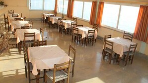 A dining area with multiple tables and chairs, large windows with curtains, and a polished floor. - El Greco Hotel by Estia (Corfu)